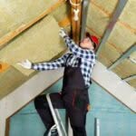 Operaio su una scala rimuove materiale isolante dal soffitto di una casa